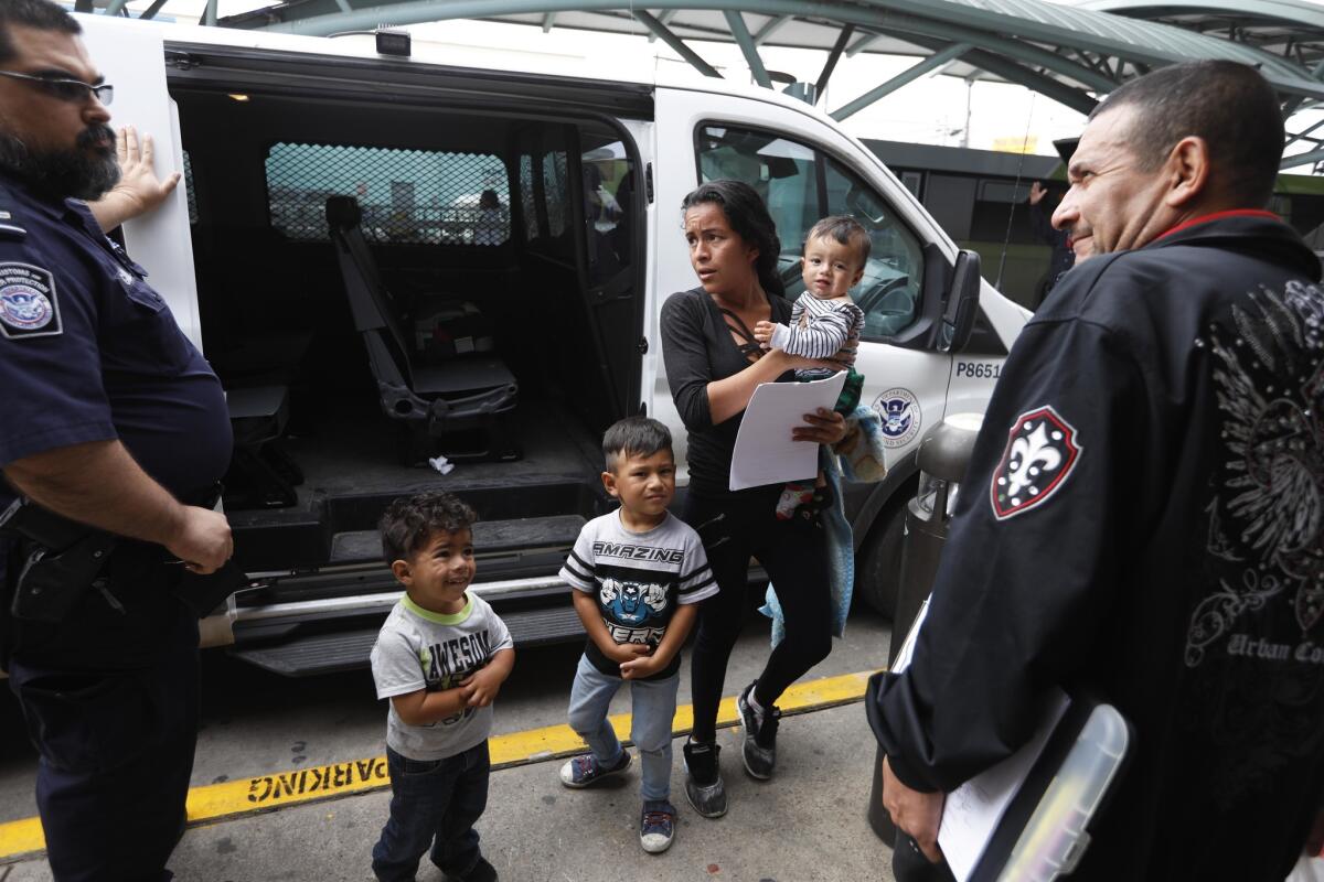 A Border Patrol agent drops off Suteig Hernandez Flores, 24, and sons Peter, 8 months old; Stanley, 4 years; and Neri, 3; at the McAllen bus station. Roland Garcia, right, with Angry Tias and Abuelas, prepares to guide them to their bus.