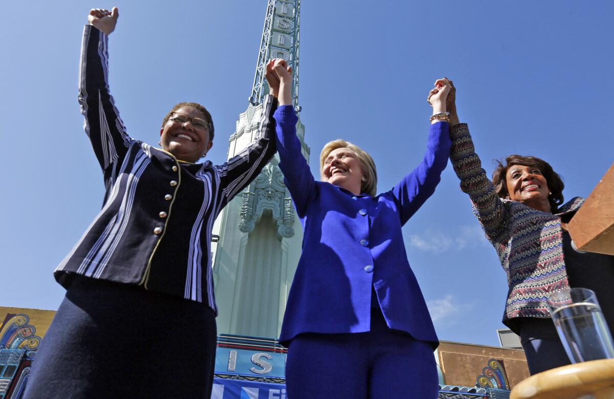 Karen Bass, Hillary Clinton and Maxine Waters hold up hands at a rally in 2016.
