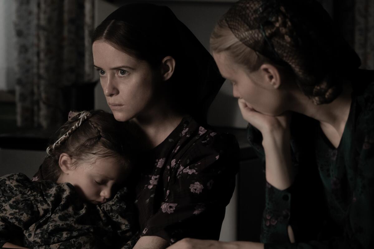 A woman comforts a child as another woman looks on in a scene from “Women Talking.”