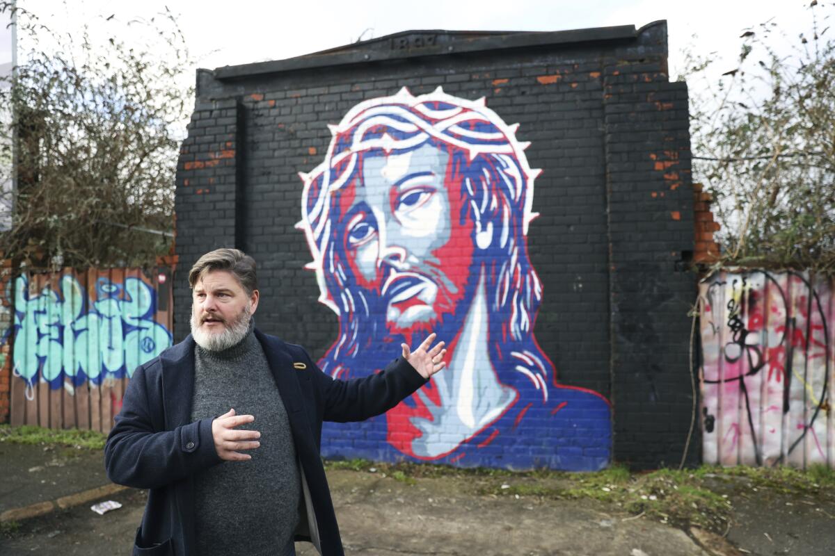 A man stands in front of a wall with a painting in west Belfast, Northern Ireland.