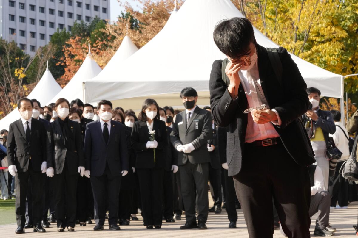 A man wiping tears stands before black-clad mourners