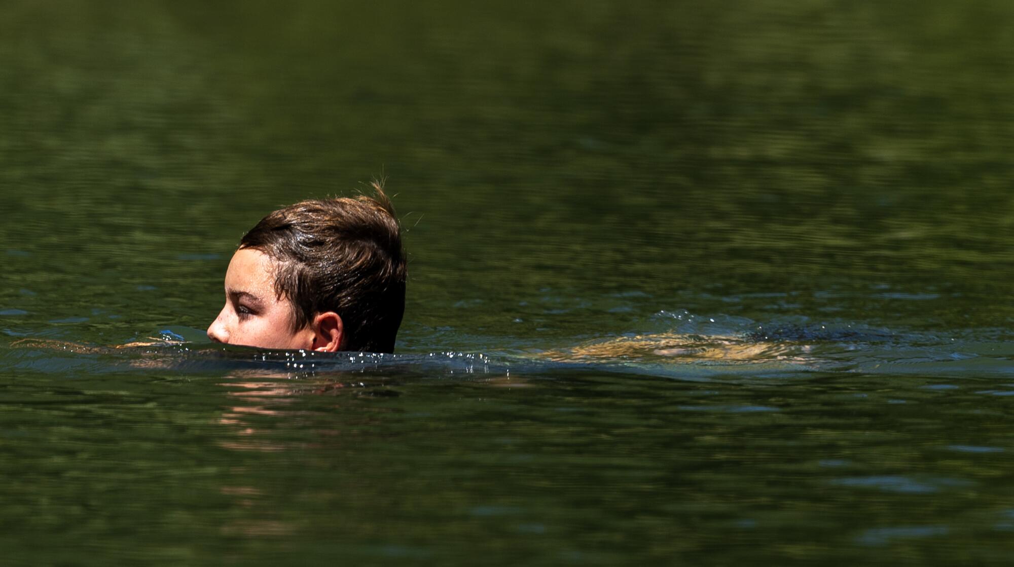 A boy swims in the Russian River, his eyes and forehead just above the water.