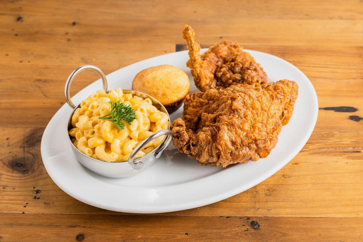 A photo of two pieces of Willie Mae's fried chicken on a plate with a side of mac and cheese and a cornbread muffin.