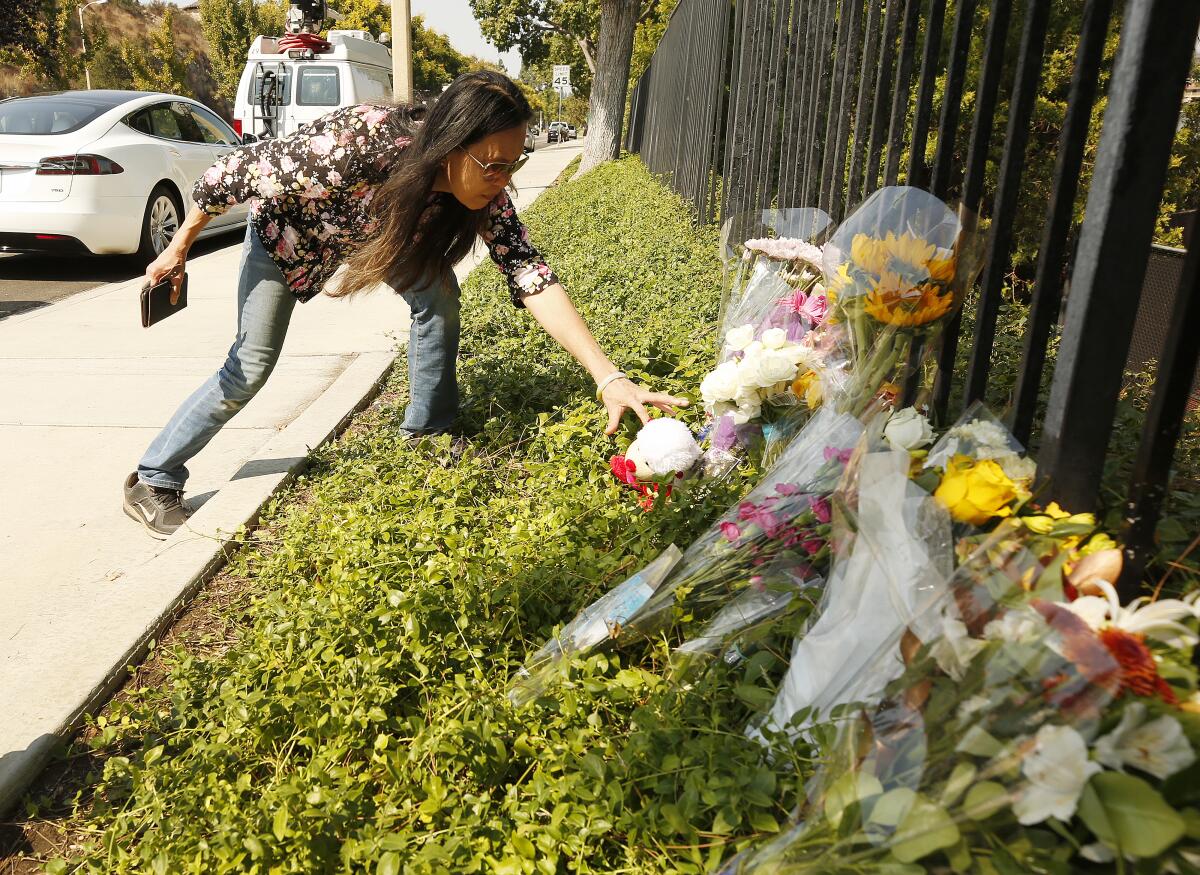 A woman adds an item to a makeshift memorial alongside a fence 