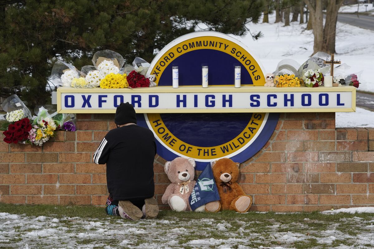A well wisher kneels to pray at a memorial on the sign of Oxford High School in Oxford, Mich., Wednesday, Dec. 1, 2021. A 15-year-old sophomore opened fire at the school, killing several students and wounding multiple other people, including a teacher. (AP Photo/Paul Sancya)