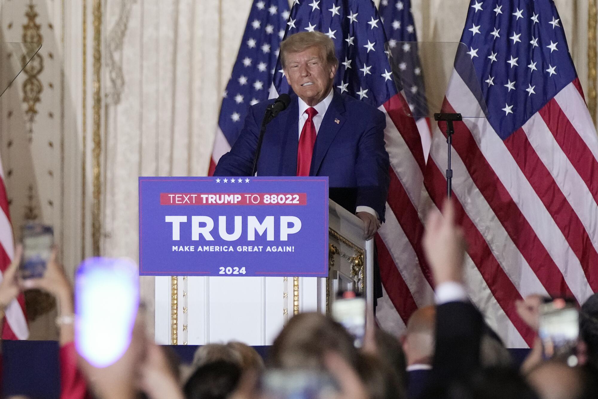 Former President Trump stands behind a lectern with a placard that reads, "Trump: Make America Great Again 2024."