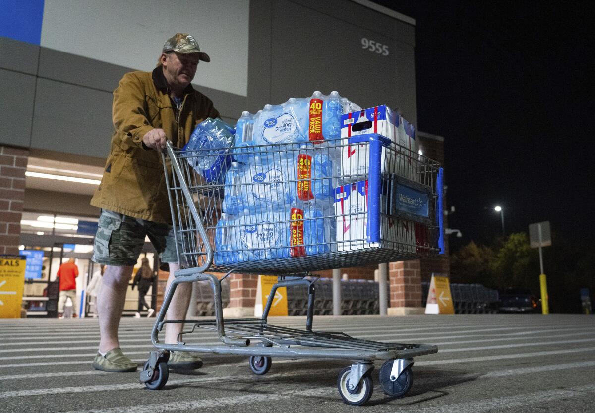 A man pushes a shopping cart full of several cases of water.
