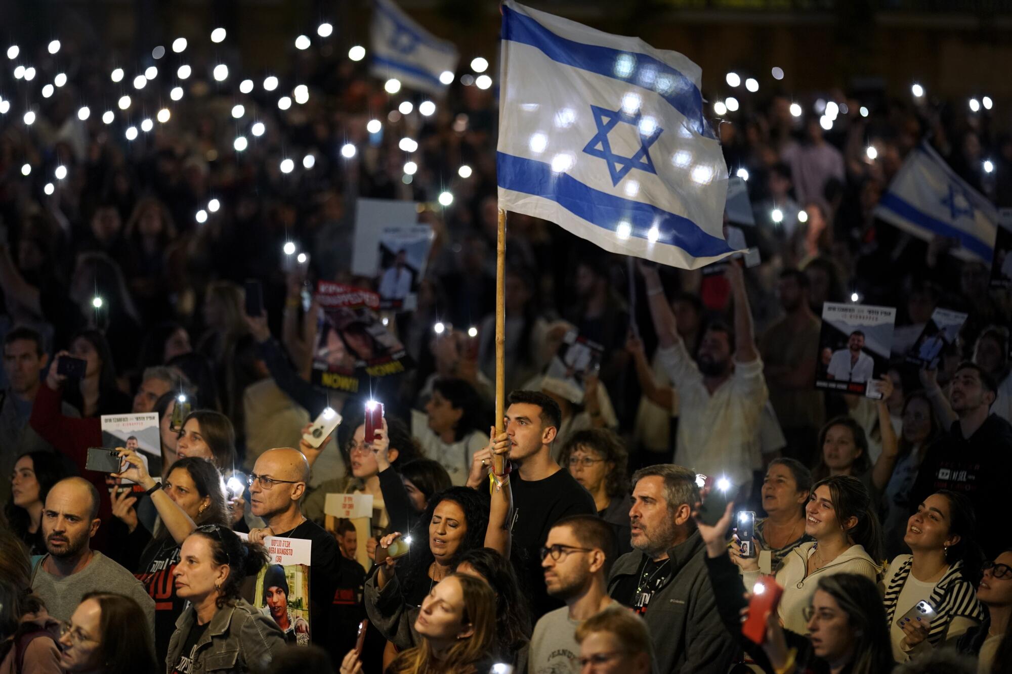 La gente sostiene luces y banderas israelíes en una protesta nocturna.  