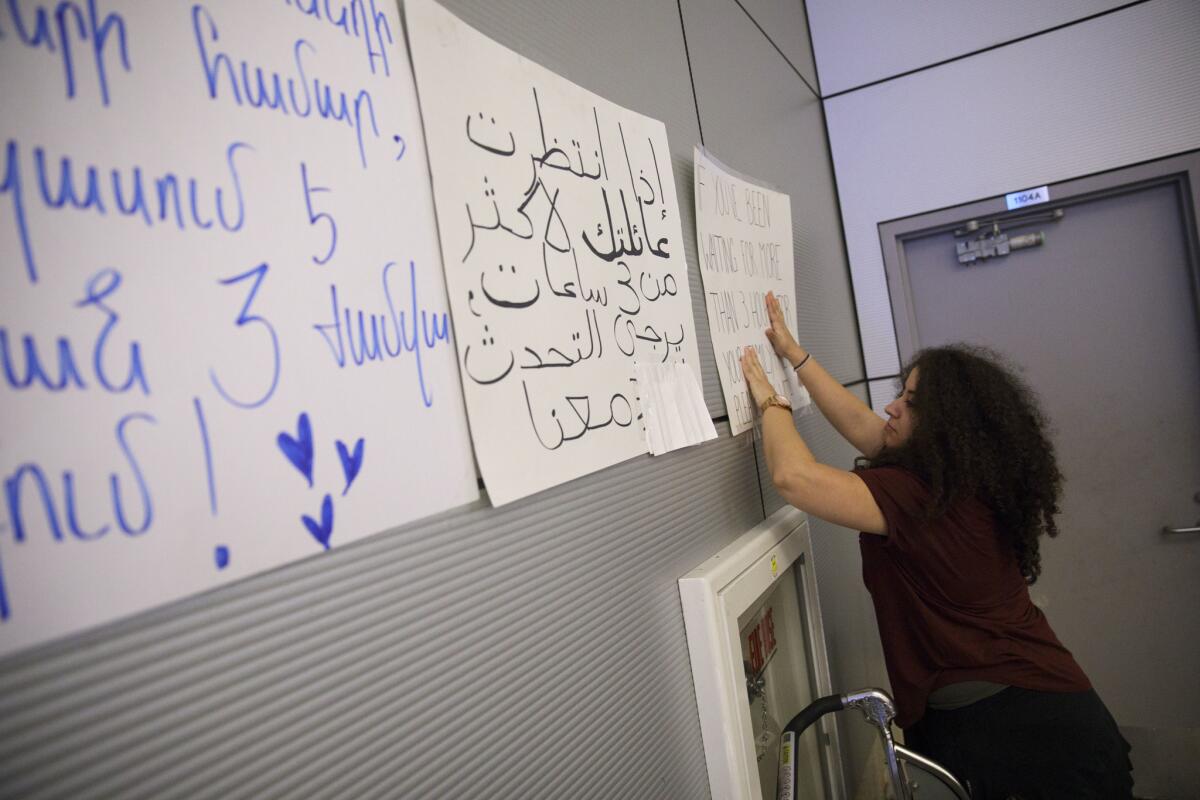Pouneh Behin, a Farsi speaker who has been volunteering at Los Angeles International Airport, hangs a sign offering help to travelers affected by President Trump's travel ban in the arrivals area of Tom Bradley International Terminal.