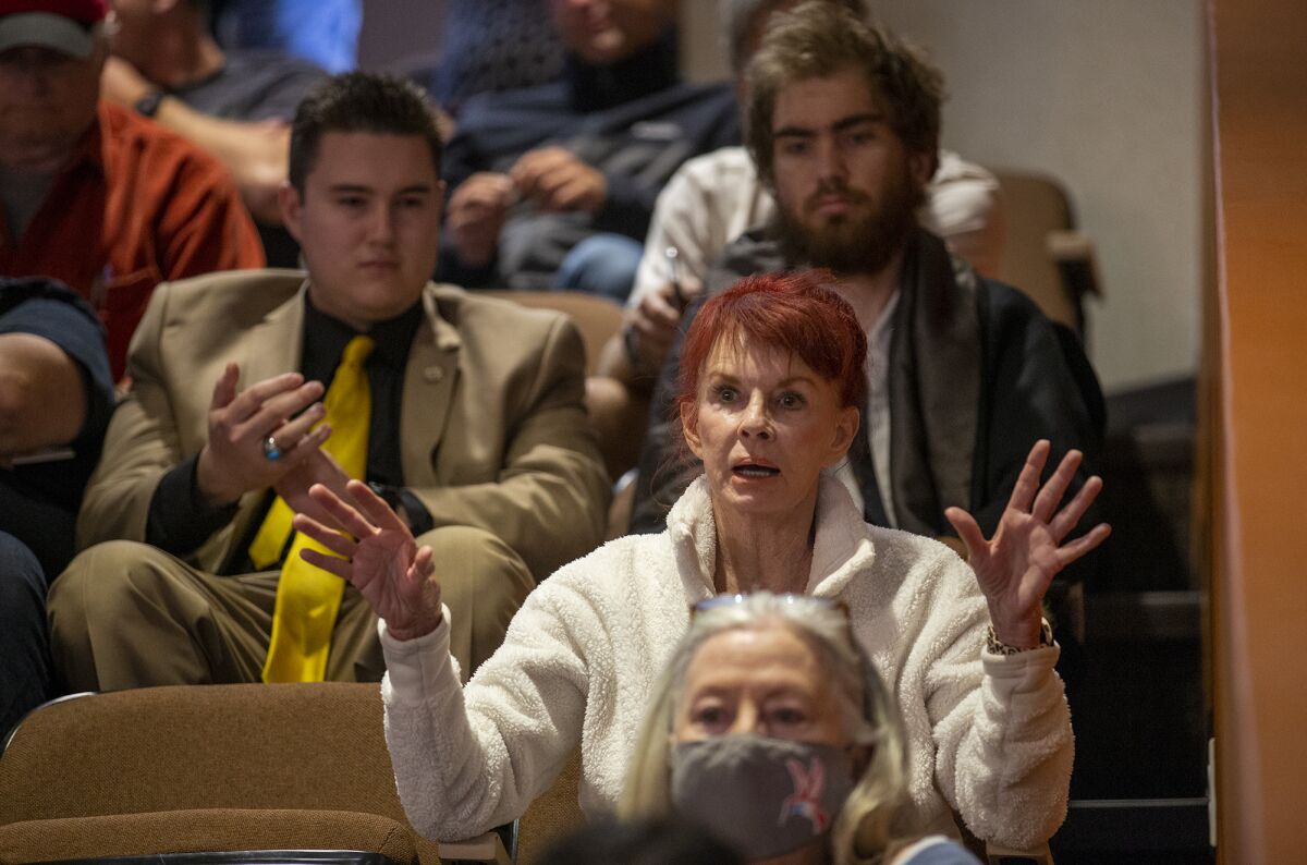 A woman sitting in an auditorium gestures with both hands while speaking
