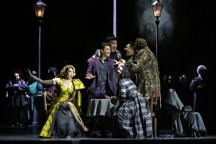 LOS ANGELES, CALIF-SEPTEMBER 12, 2019: at table, Erica Petrocelli, seated left, Saimir Pirgu, standing center with hand out, and Marina Cotsta-Jackson, seated in plaid dress, perform during an L.A. Opera dress rehearsal for Barrie Kosky's La Bohéme at the Dorothy Chandler Pavilion on September 12, 2019 in Los Angeles, California. (Photo By Dania Maxwell / Los Angeles Times)