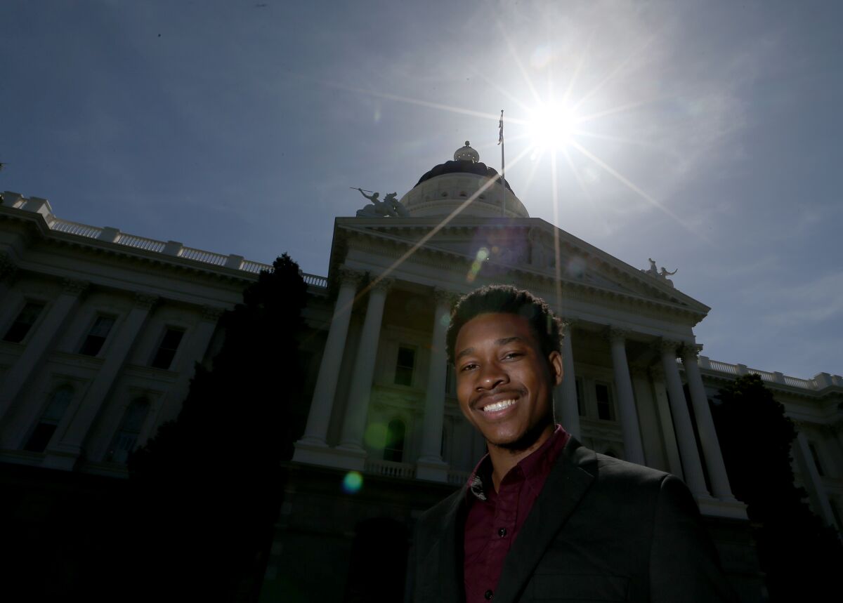 A smiling Jaheim Smith standing in a suit with the  state Capitol behind him