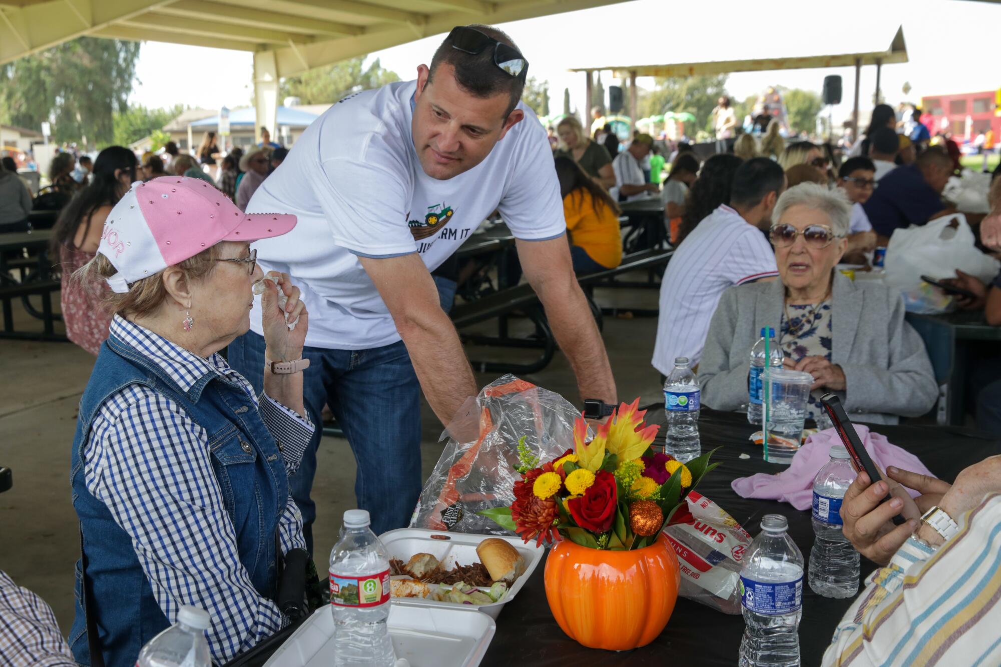 Rep. David Valadao, 45, leans over a table and talks to two older white women at a farm festival.