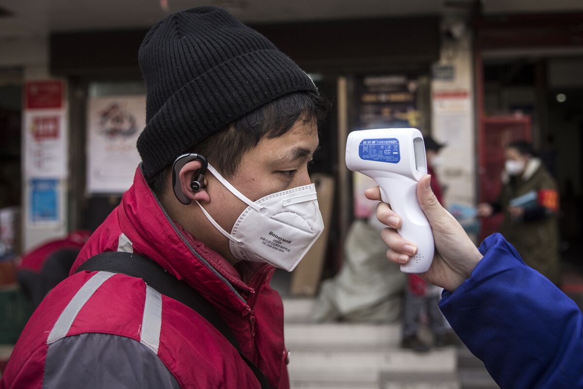 A community worker checks the temperature of courier in an Express station last month in Hubei Province, Wuhan, China.