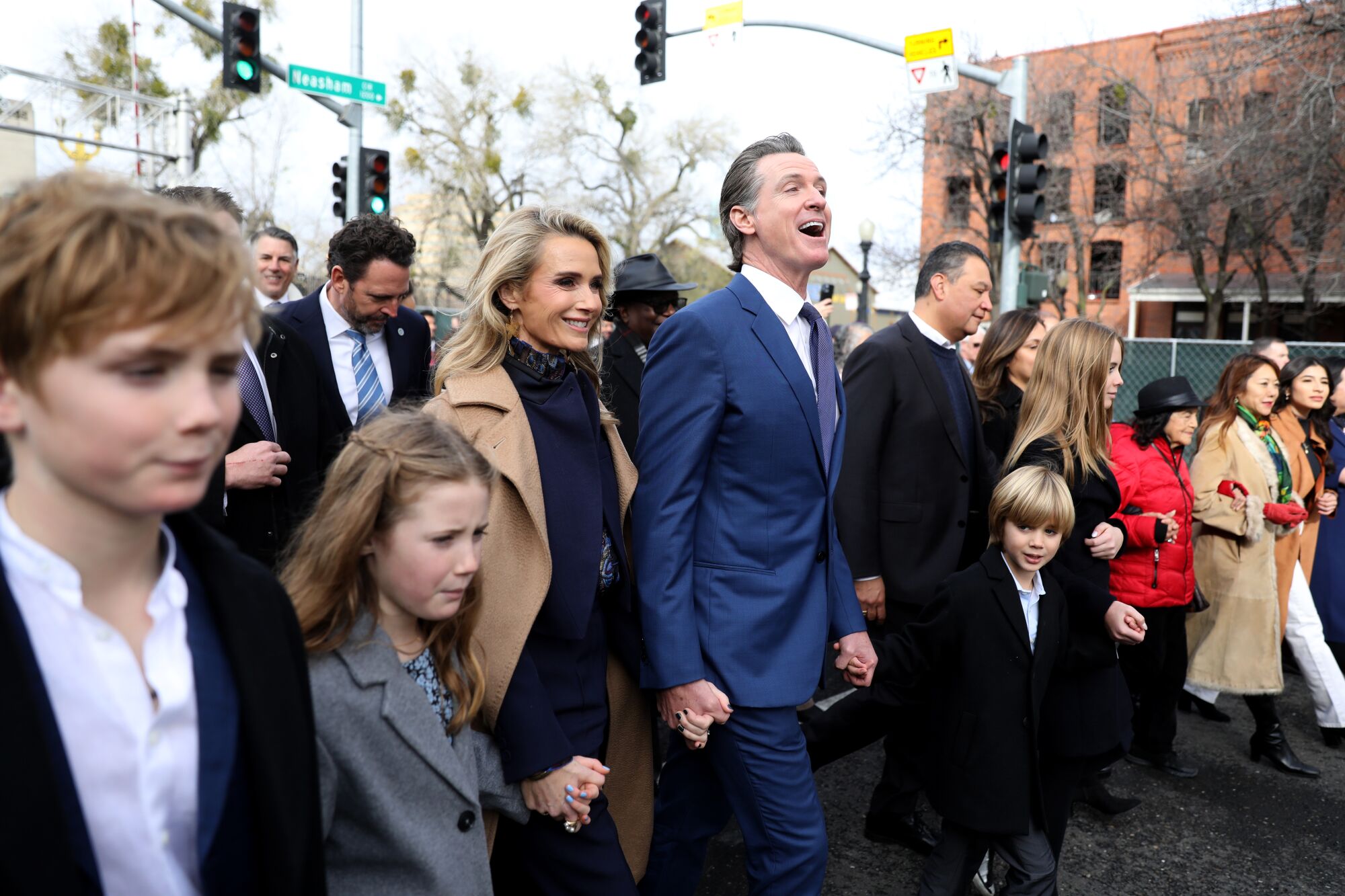 Gouverneur Gavin Newsom und seine Familie gehen mit einer Menschenmenge, die sich an den Händen hält.