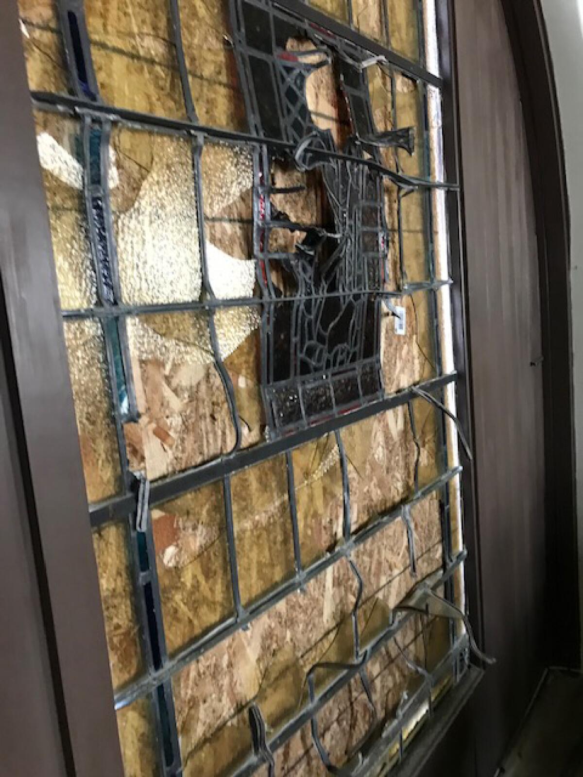 Smashed stained glass window that is boarded up.