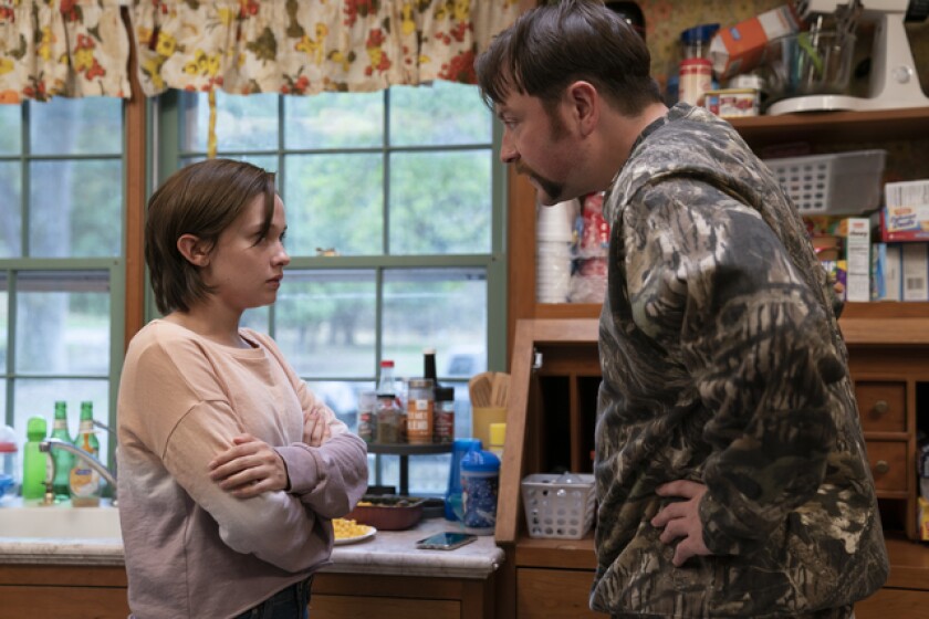 A man in camouflage confronts his daughter, wearing pink, in their kitchen