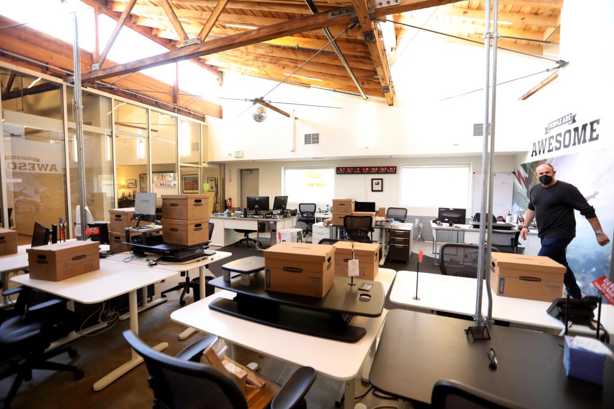 A man in an office with boxes atop desks. 