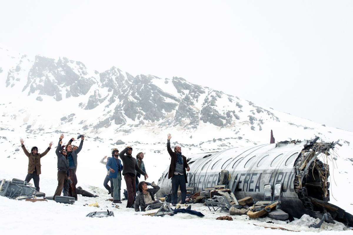 Men standing by their crashed airplane remains in snowy mountains look to the sky and wave 
