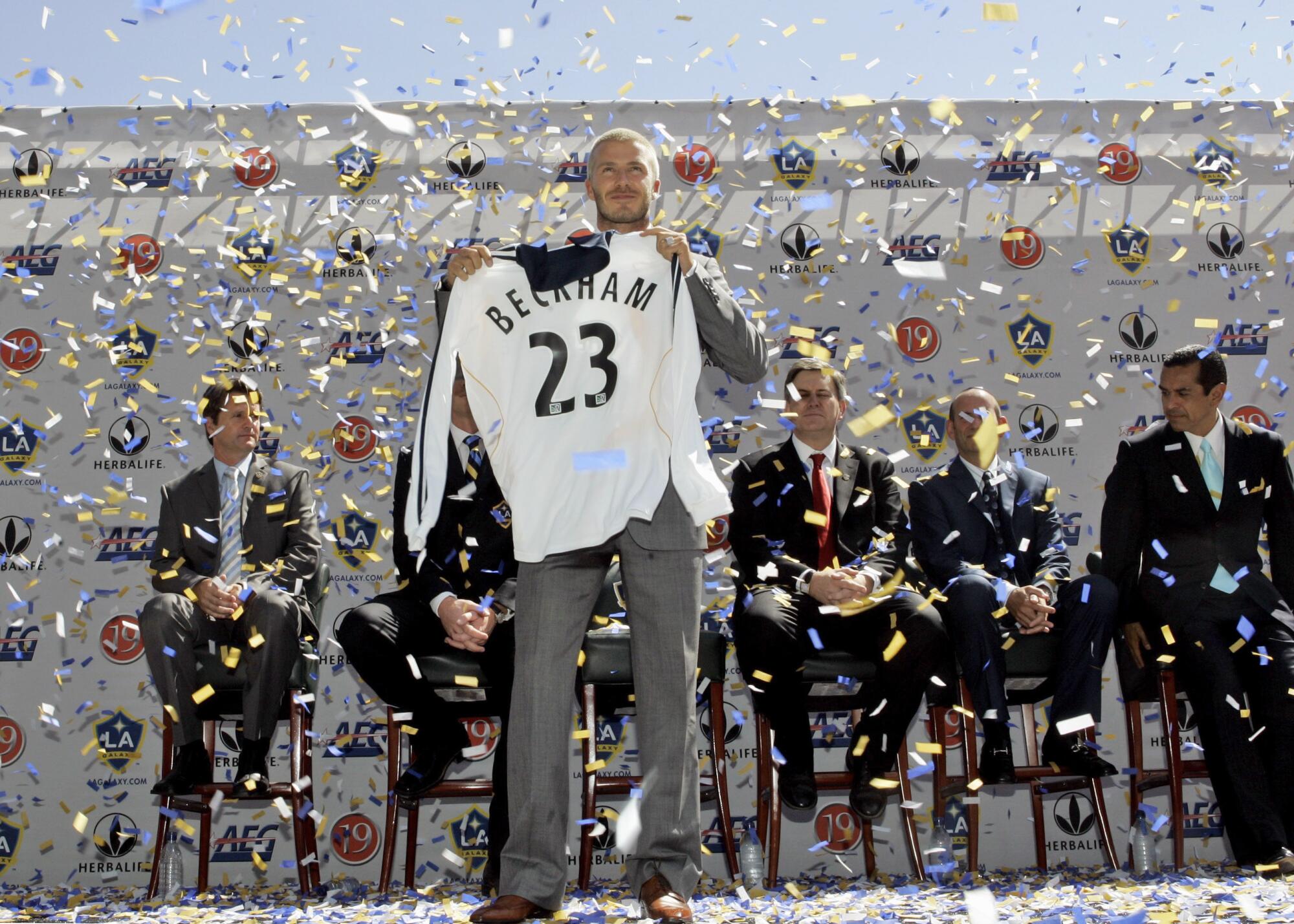 David Beckham holds up his new jersey while confetti falls.