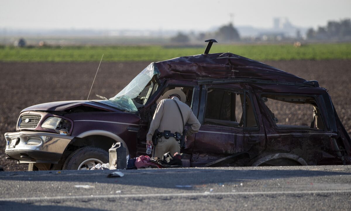 An officer looks inside driver side window of a wrecked vehicle