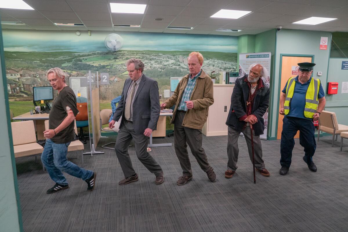 Five men in an office stand in a line and look to their right.