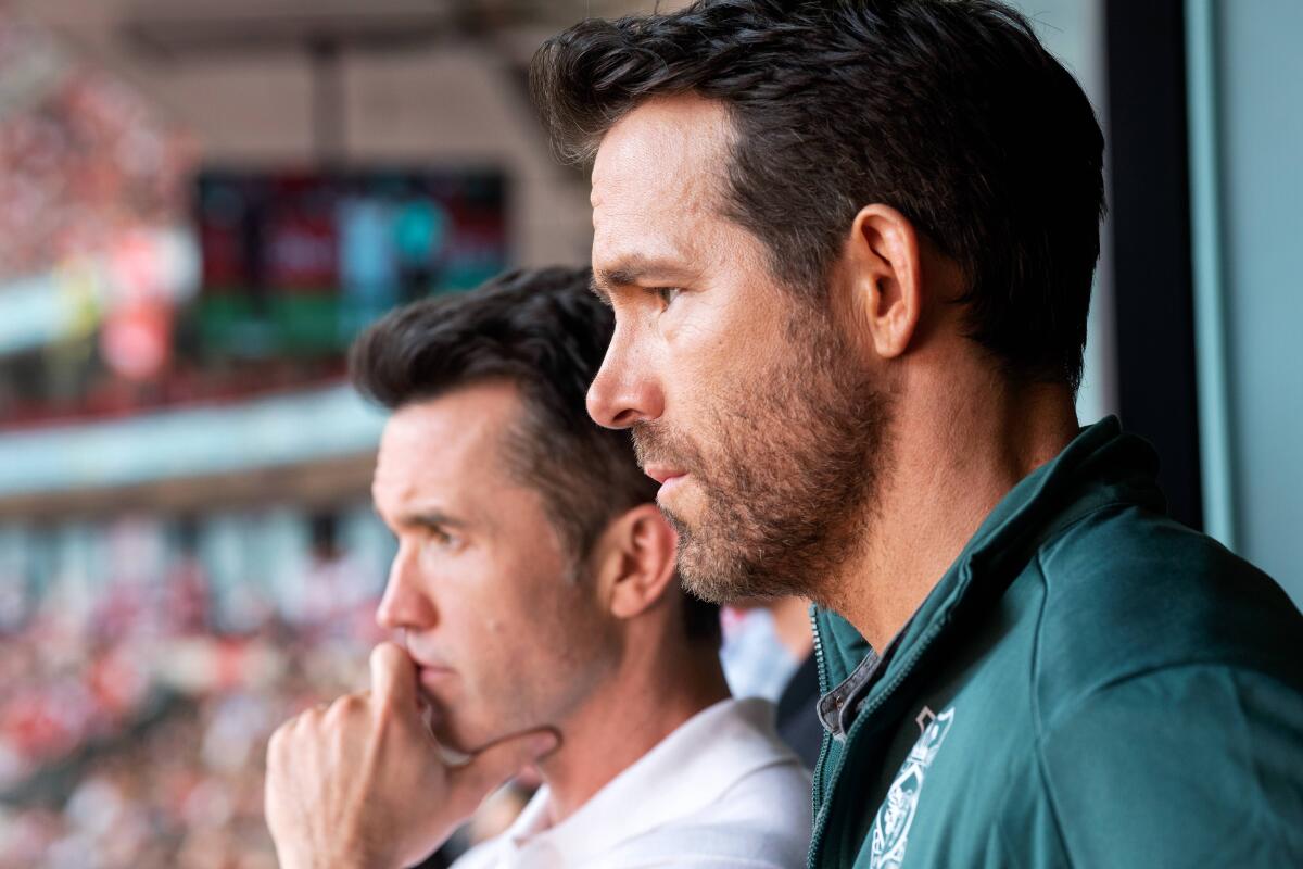 Two men in a stadium box looking down on the field.