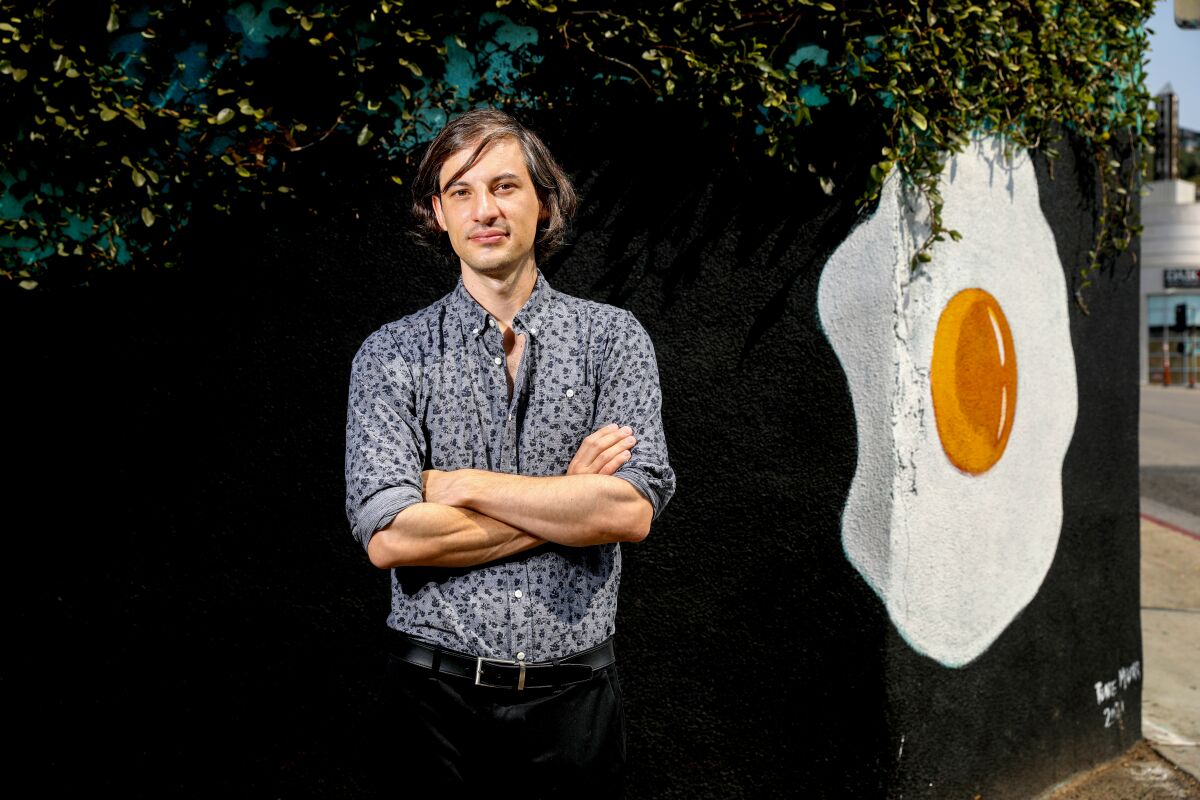 A young man stands in front of a mural of a fried egg on a black background.