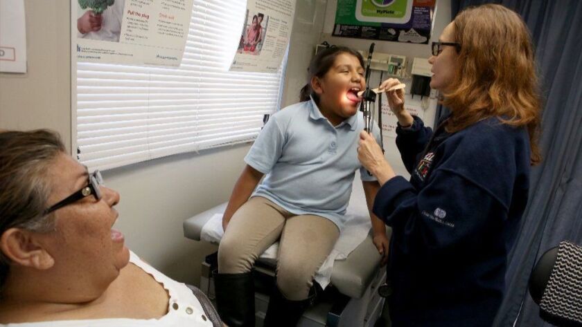 Carmen Sanchez, left, watches as her 8-year-old daughter, Dafne, gets a checkup from nurse practitioner Anne Traynor at a Cedars Sinai mobile clinic that visited the Jordan Downs housing project in Los Angeles in 2015.