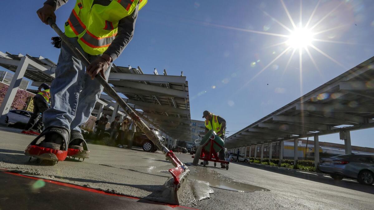 Juan Reyes, left, and Devin Vestal apply a cool pavement material to a parking lot in downtown Los Angeles. City officials hope the pavement will help cool the city and mitigate the effects of climate change.