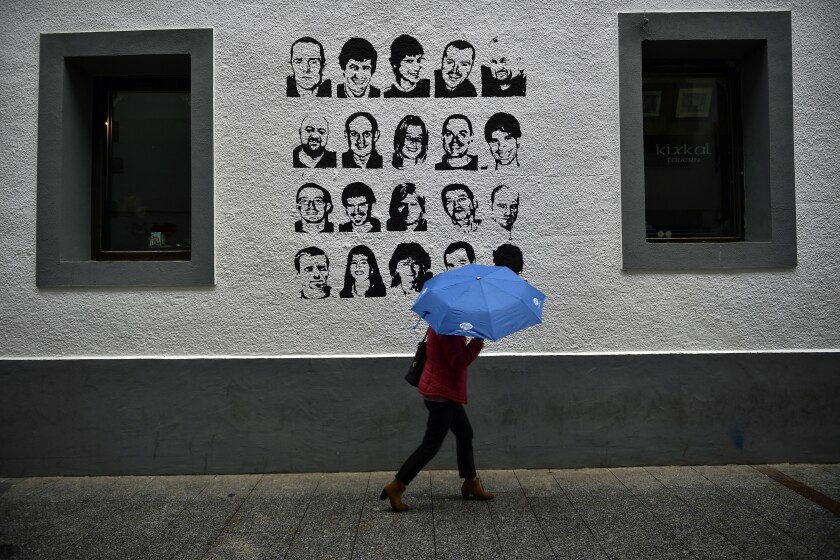 A woman with an umbrella walks past a wall painted with portraits of prisoners of the Basque separatist armed group ETA.