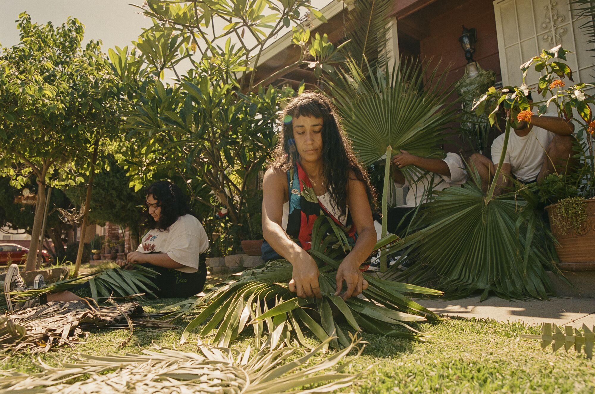 Plusieurs personnes sont assises sur l'herbe, coupant et tissant des palmiers.