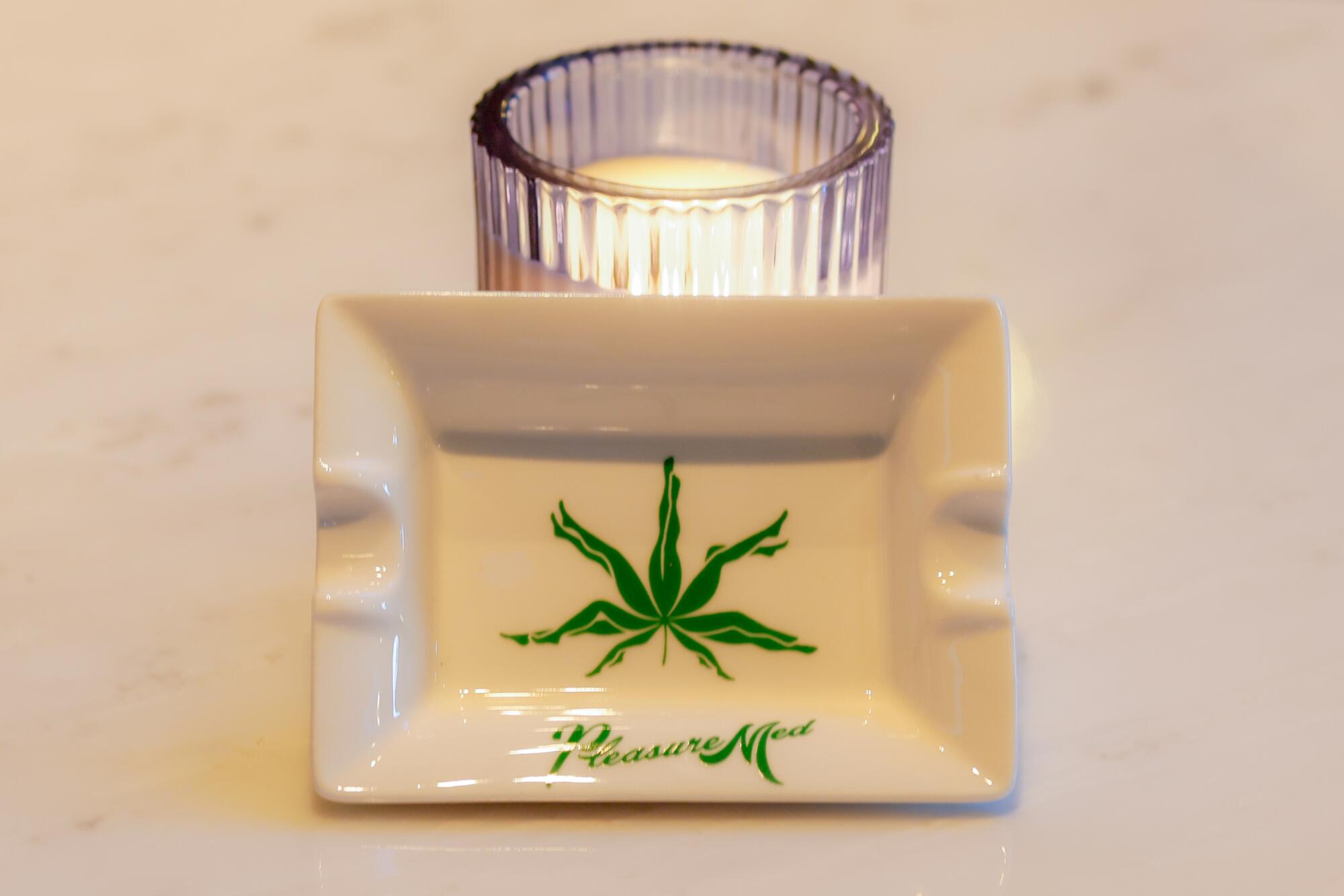 A white ceramic ashtray with a pot-leaf-and-legs logo and the word PleasureMed.