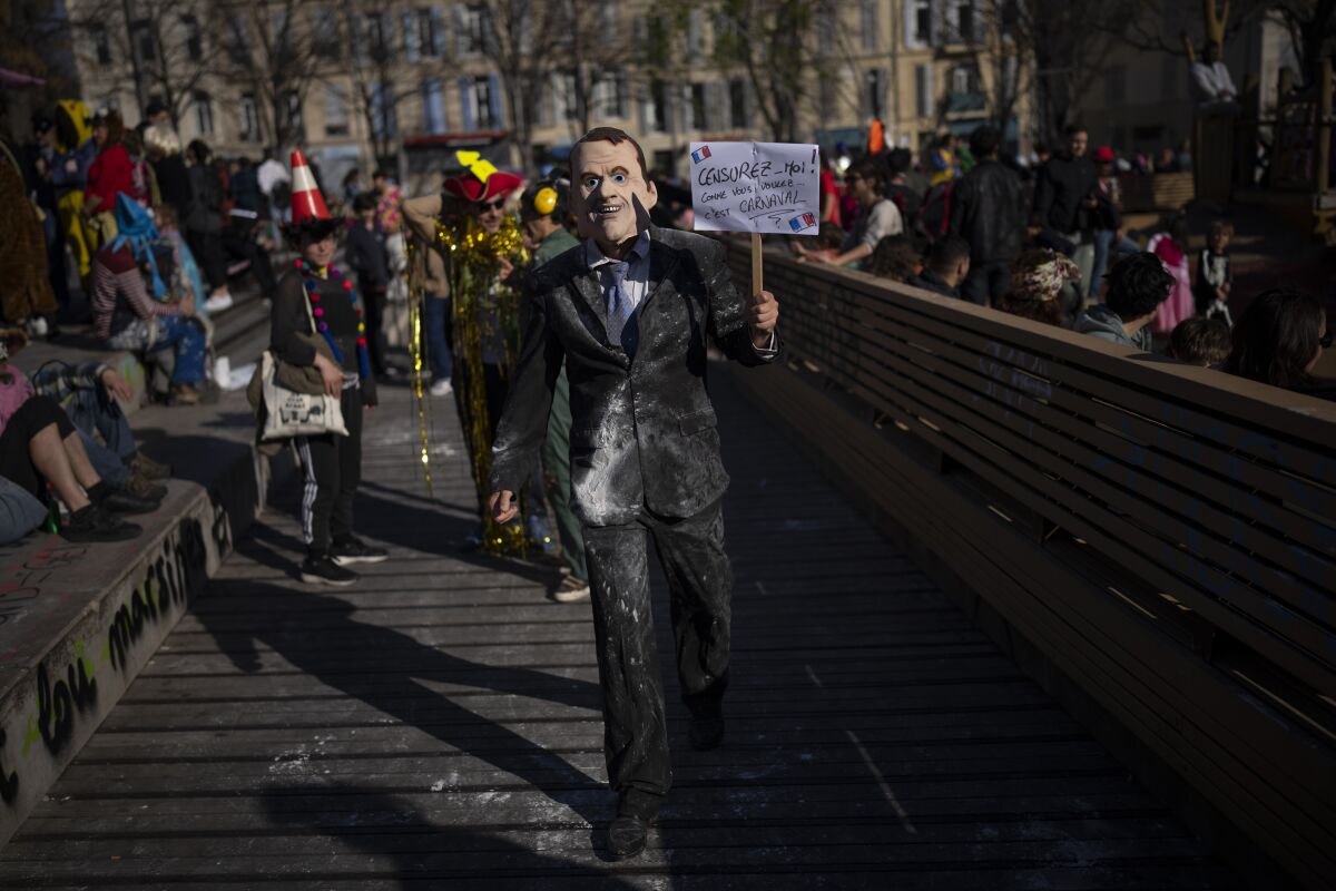 A man wearing a mask depicting French President Emmanuel Macron holds a sign reading "censor me however you want, it is carnaval" during Marseille's Carnaval de la Plaine in Marseille, southern France, Sunday, March 19, 2023. The city's unofficial yet infamous Carnaval de la Plaine had arrived — right on the precipice of a week filled with violent protests and discontent over French President Emmanuel Macron's move to force through an unpopular bill raising the retirement age to 64.(AP Photo/Daniel Cole)