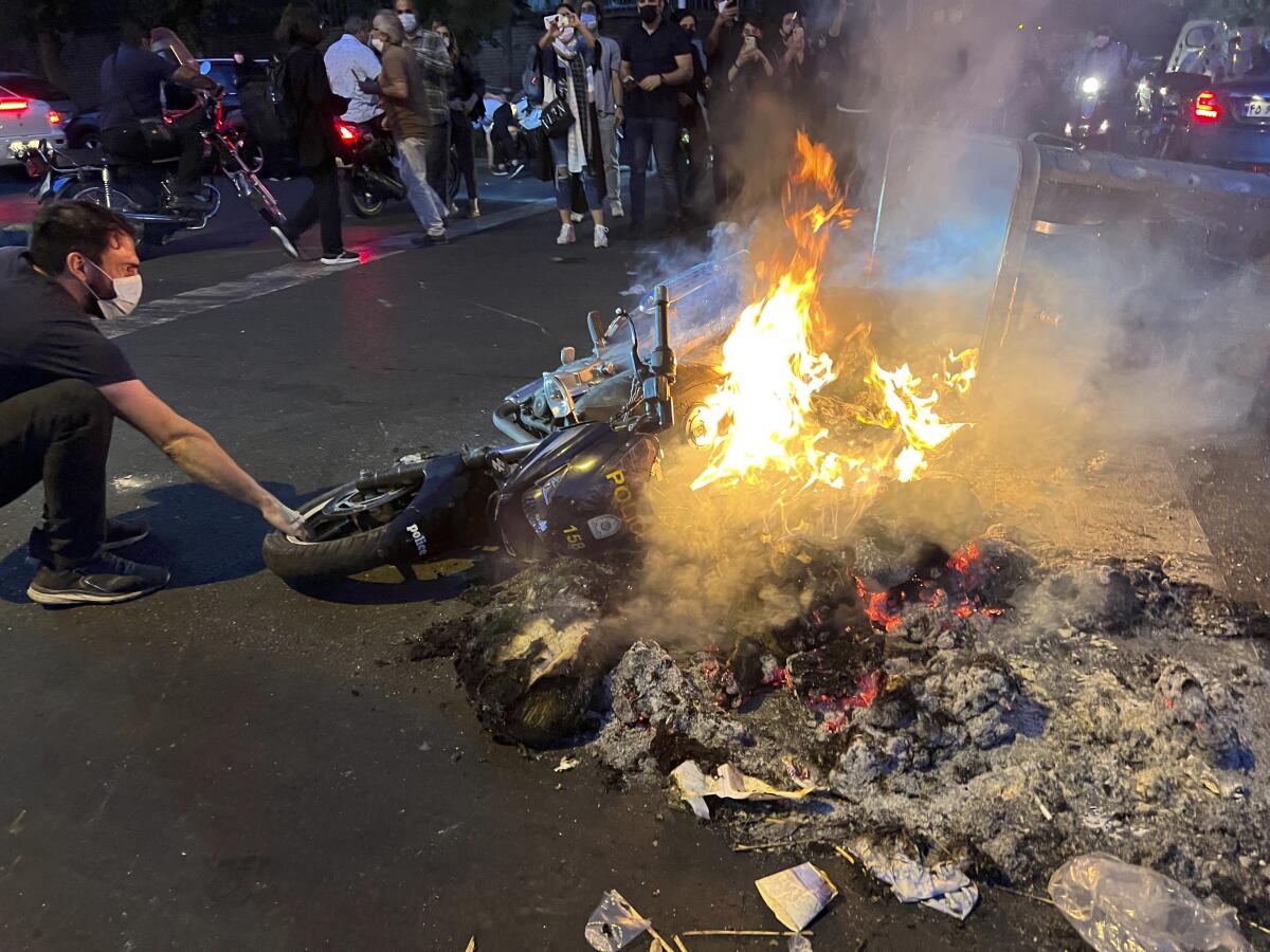 A man touches a police motorcycle which is set on fire during a protest.