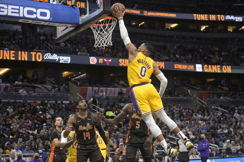 Russell Westbrook (0), base de los Lakers de Los Ángeles, se dispone a clavar el balón frente a Gary Harris (14) y Mo Bamba (5), del Magic de Orlando, durante la primera mitad del juego de la NBA, el viernes 21 de enero de 2022, en Orlando, Florida. (AP Foto/Phelan M. Ebenhack)