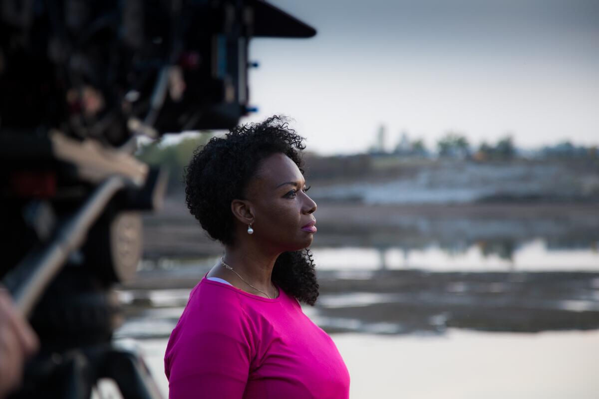 A woman in a pink shirt looks out over a segment of the Arkansas River as a camera observes