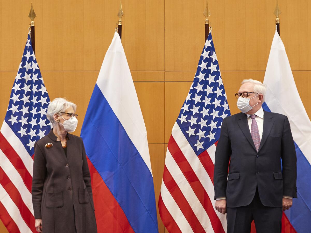 A woman and a man in suits standing before U.S. and Russian flags