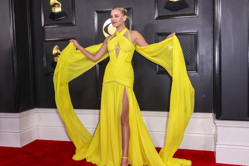 A woman in a draped yellow gown poses on a red carpet