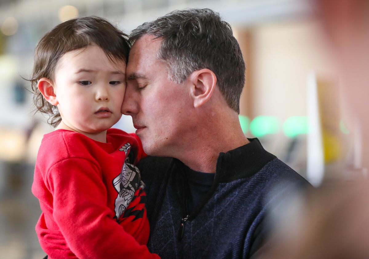 Ken Burnett holds his son, Rowan, 3, at San Diego International Airport. Rowan, his sister, Mia, 1, and their mom, Yanjun Wei, were returning to San Diego after quarantine at Travis Air Force Base. Ken Burnett, who was not an evacuee, traveled home with them from Sacramento.