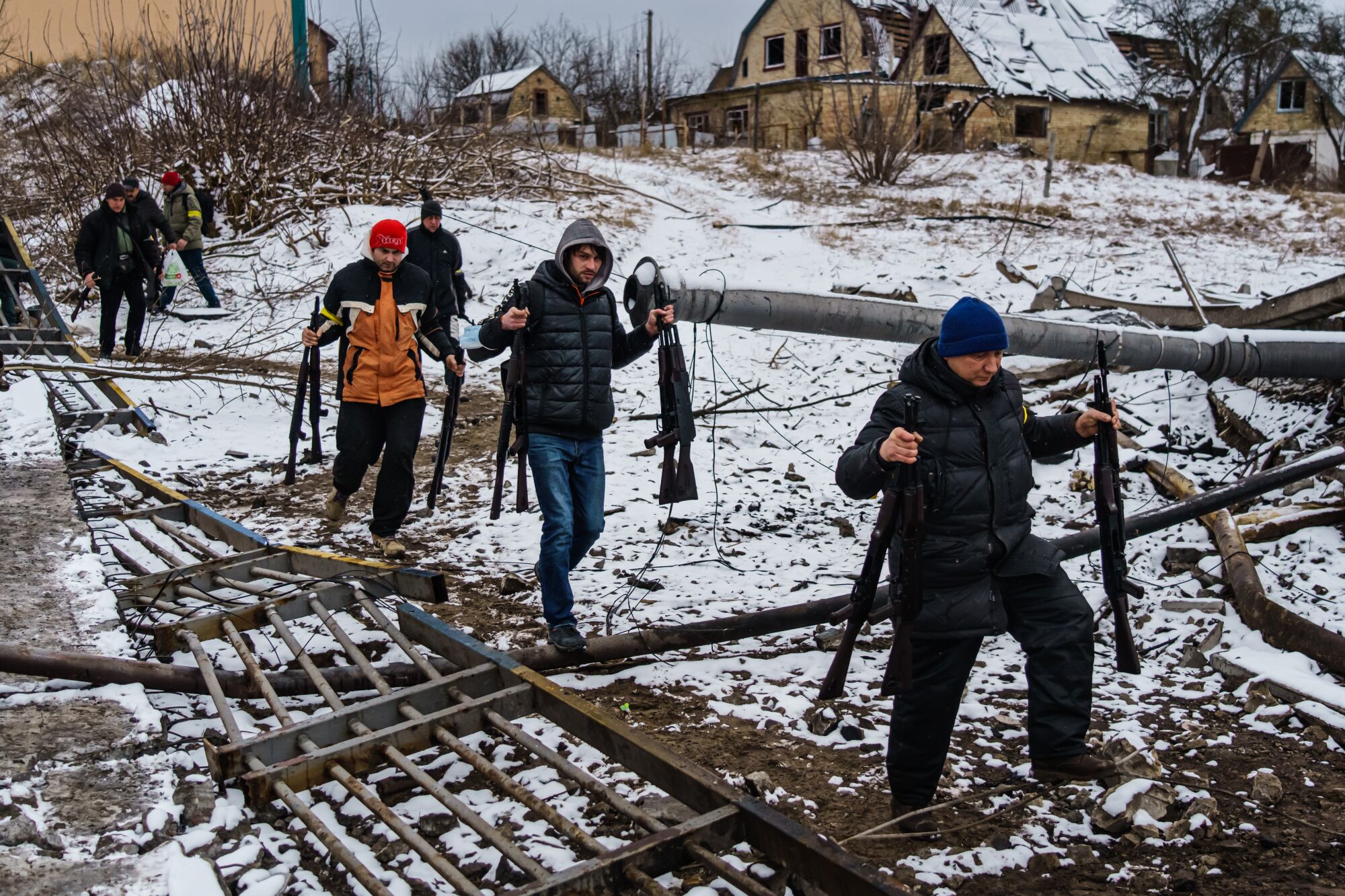 Volunteer fighters transport rifles across a river under a destroyed bridge to reinforce Ukrainian troops in Irpin