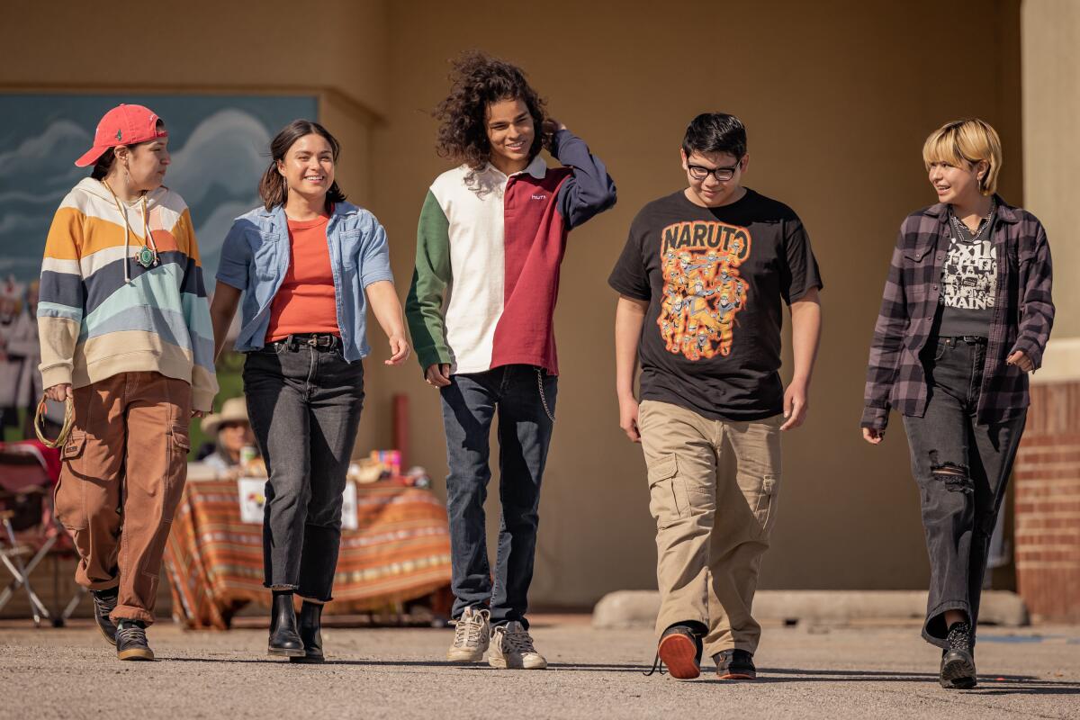 A group of teenagers walk toward the camera five across