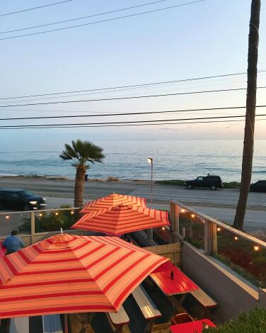 A vertical photo of umbrellas and bulb lights on the patio of Malibu Seafood overlooking PCH and the ocean.