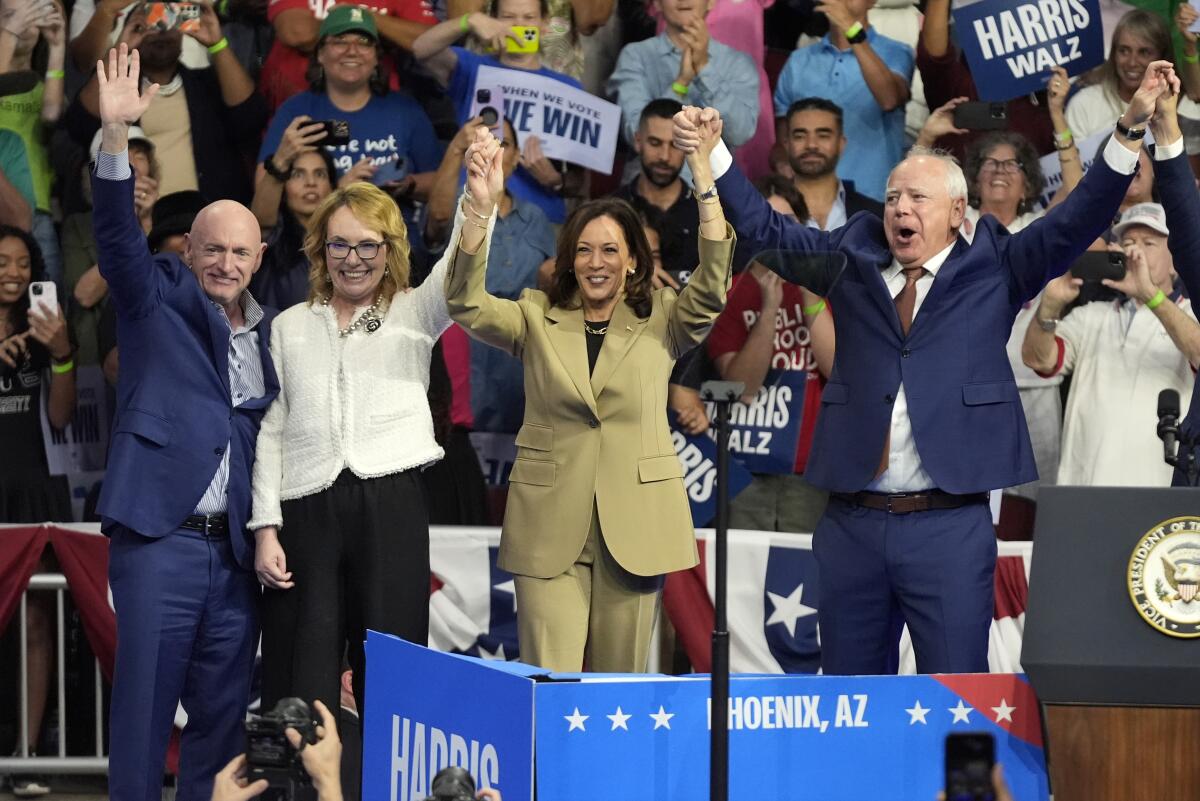 Two women and two men hold raised hands on a rally stage. 