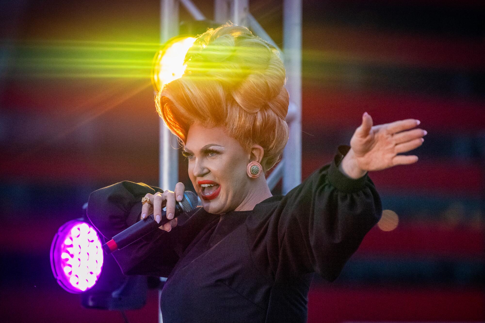 A drag performer on stage holding a microphone in one hand.