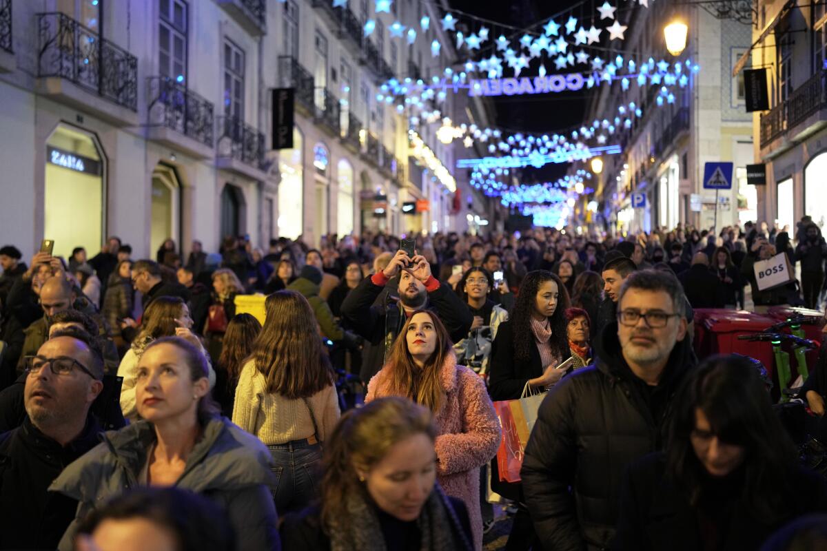 People look up at Christmas lights while strolling around downtown Lisbon's Chiado neighborhood on Dec. 23, 2023. 