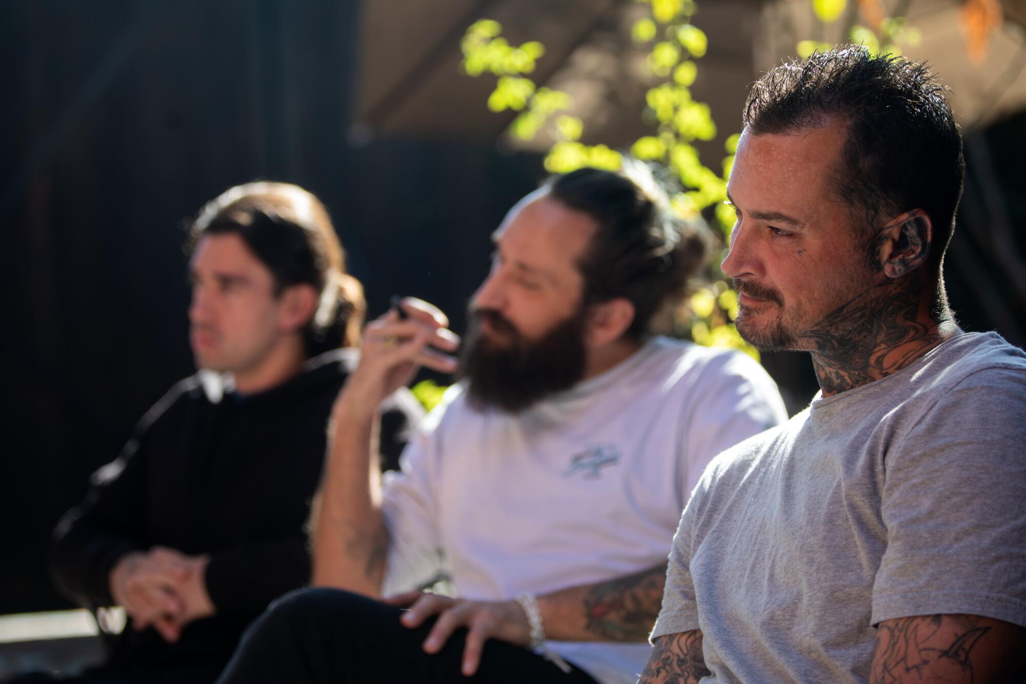 Sunlight hits green leaves behind three men seated outdoors