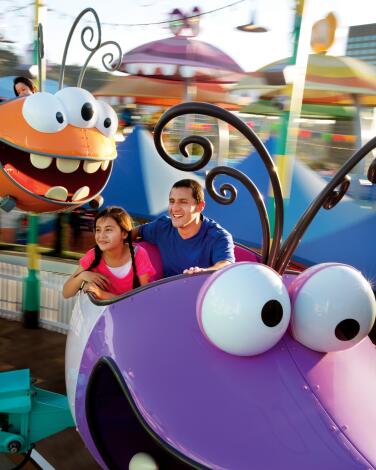 A child and an adult ride in colorful insect-shaped cars on a theme park ride