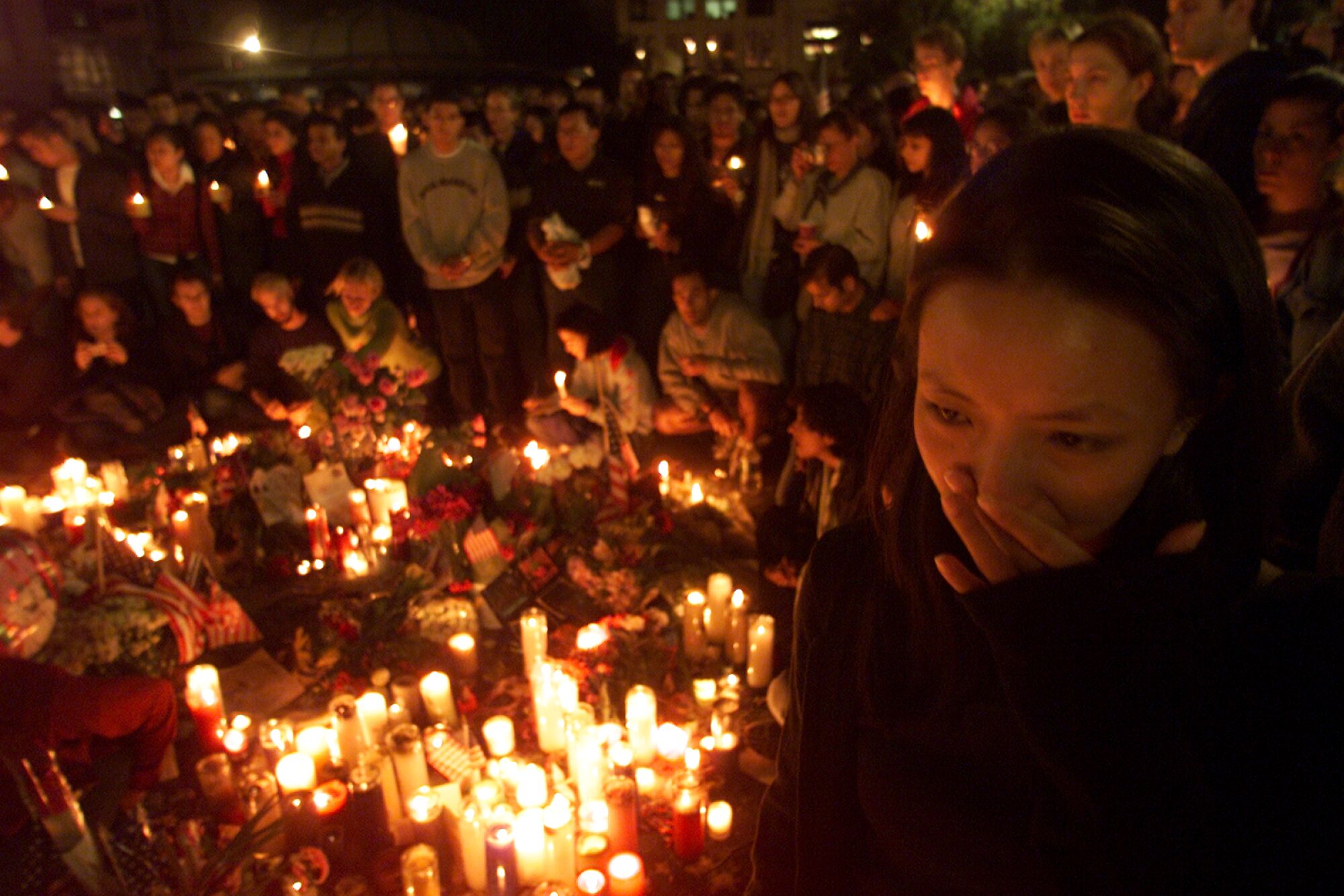 A woman, left foreground, stands among a group encircling candles and flowers