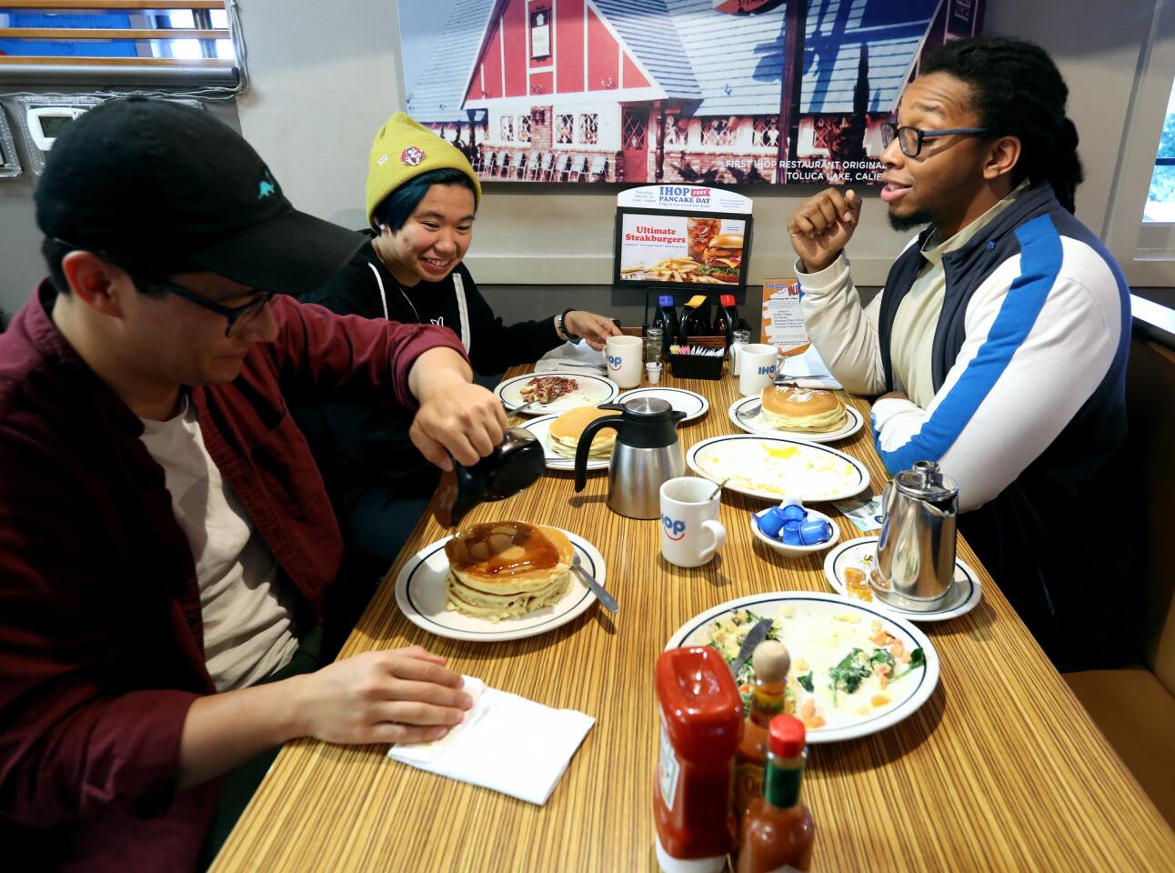 Lester Knight, 28, pours syrup on his free pancakes while having breakfast with friends Gizelle Orbino, 31, center, and Melvin Young, 31, all from Burbank, during the IHOP free pancake day, at the location on San Fernando Rd, in Burbank on Tuesday, March 12, 2019.